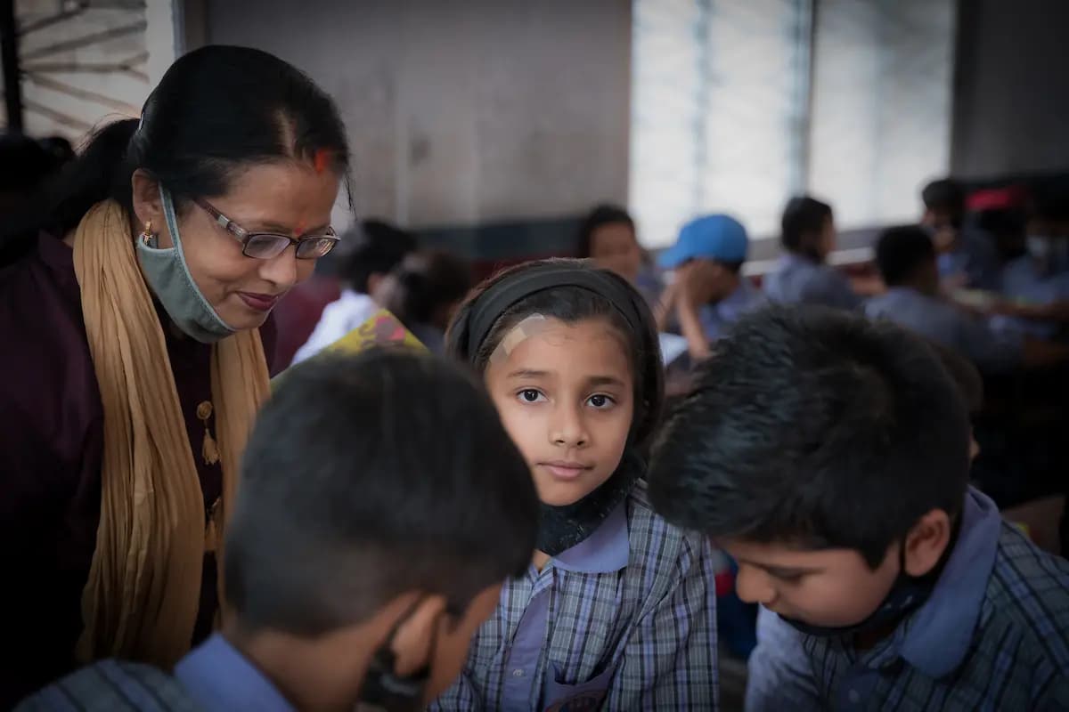 A teacher leaning in to guide a group of students